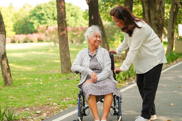 Verzorger helpt en ondersteunt aziatische senior of oudere oude dame vrouw patiënt op rolstoel in park gezond sterk medisch concept