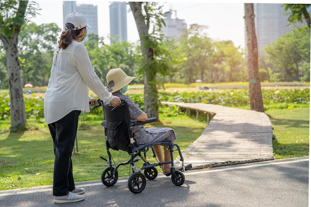 Verzorger hulp en zorg Aziatische senior of oudere oude dame vrouw patiënt zittend op rolstoel in park gezond sterk medisch concept