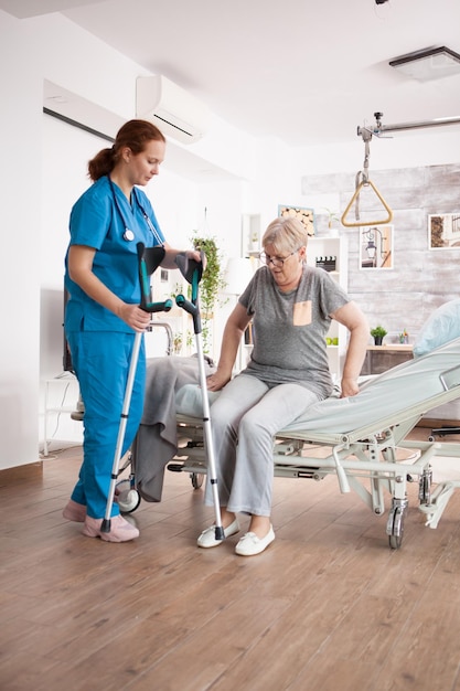 Verzorger in verpleeghuis die oude vrouw helpt te lopen met krukken.