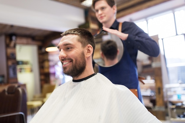 verzorging, kapsel en mensenconcept - man en haarstylist of kapper met spiegel bij kapperszaak