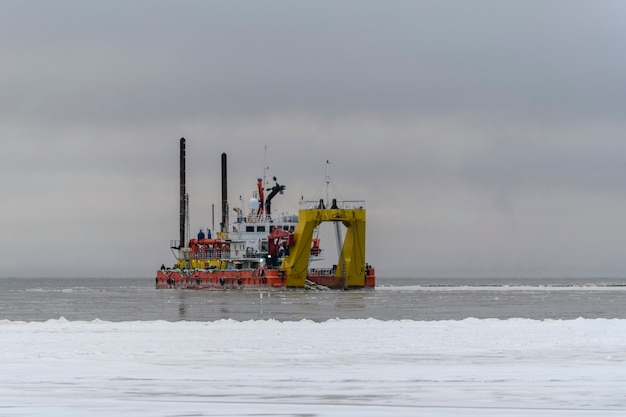 Vessel engaged in dredging at sunset time. Hopper dredger working at sea. Ship excavating material from a water environment.