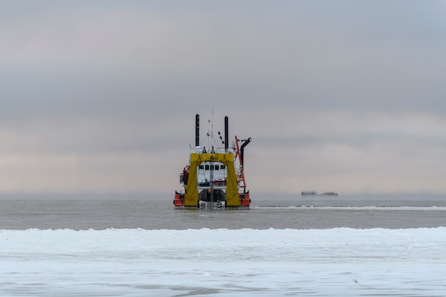 Vessel engaged in dredging at sunset time. Hopper dredger working at sea. Ship excavating material from a water environment.