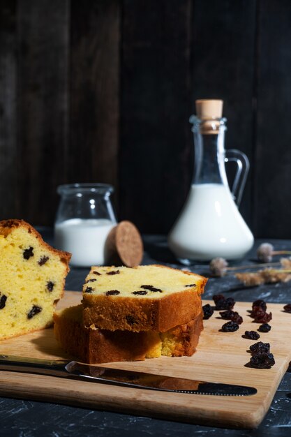  a vessel with milk stands on an old wooden background, near a cake with raisins