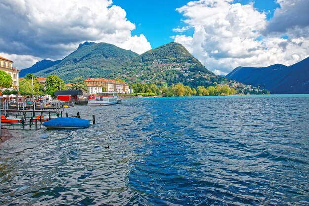 Vessels at the landing stage at the promenade of the luxurious resort in Lugano on Lake Lugano and Alps mountains in Ticino canton of Switzerland.