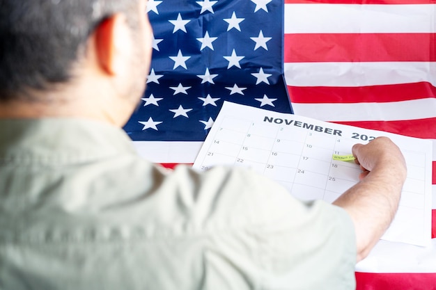 Veteraan die de kalender van Veteranendag markeert met de Amerikaanse vlag op de achtergrond