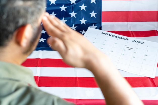 Veteran salutes the U.S. flag next to a calendar marking Veterans Day