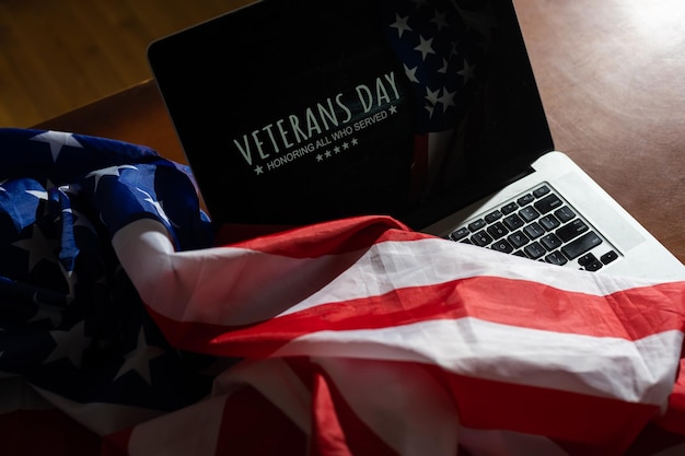 Giorno dei veterani scritto in laptop con bandiera degli stati uniti, su un fondo di legno rustico