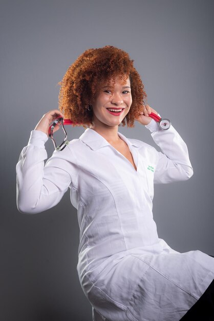 Photo veterinarian woman beautiful with red hair in white uniform and holding a stethoscope animal care isolated on gray background