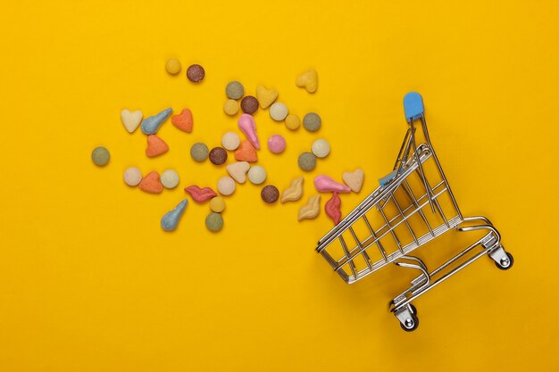 Veterinary tablets of vitamins with different shapes for cats and shopping trolley on a yellow