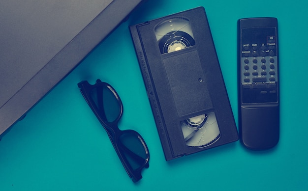 Vhs player, video cassette, 3d glasses, tv remote on a blue surface