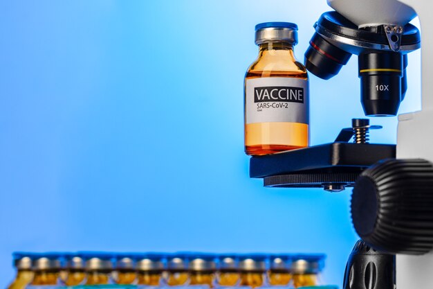 Vial of Covid-19 vaccine next to a microscope