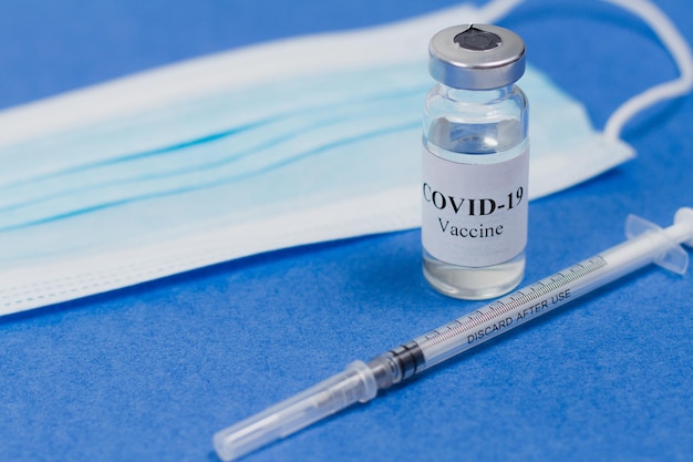 Vial of Covid19 vaccine a syringe for injection and a blue mask on a blue background SARSCoV2 vaccination treatment