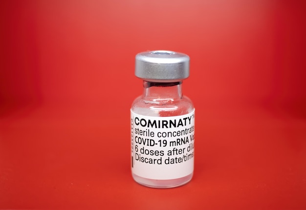 a vial of the pfizer vaccine against sars cov-19, covid, coronavirus on a red background