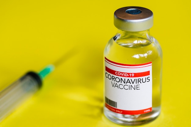 Vial with Coronavirus Covid-19 vaccine with syringe in yellow background. Healthcare and medical concept. Copy space for text