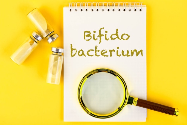 Vials, ampoules with dry probiotic, bifidobacteria, with probiotic powder inside on a yellow background. Text, magnifying glass.