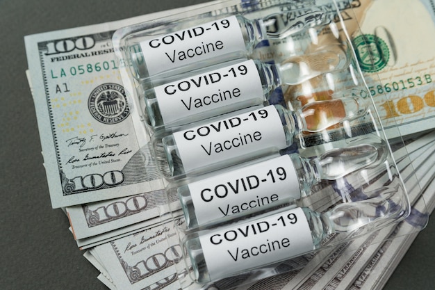 Photo vials of vaccine from covid-19 lie on stack of money. expensive drugs for coronavirus