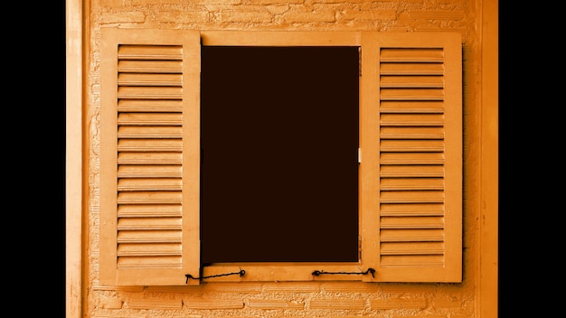 Яркое деревянное окно оранжевого цвета с открывающимися ставнями на кирпичной стене