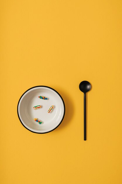 Vibrant colorful flat lay of medicine pill capsules filled with sugar candy sprinkles on yellow background. Creative concept of overdose medicine usage and addiction to food supplement.