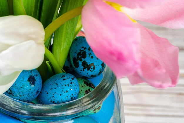 Vibrant Easter eggs with flowers in a glass jar close up, cropped image