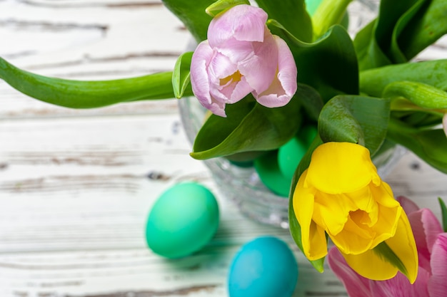 Vibrant Easter eggs with flowers in a glass jar close up, cropped image