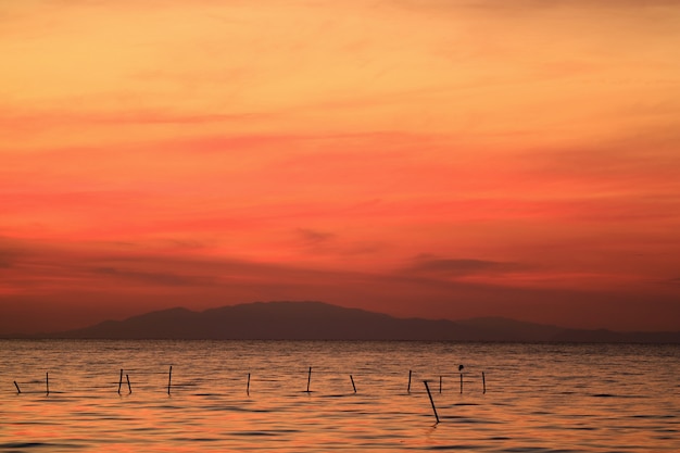 Vibrant Orange Color Sunrise Sky over the Sea with Silhouette of a Bird Perching on the Pole