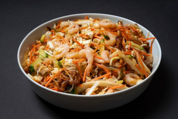 Foto piatto vibrante di insalata di gamberi. insalata tradizionale di gamberi con verdure. ciotola colorata con frutti di mare su sfondo nero.