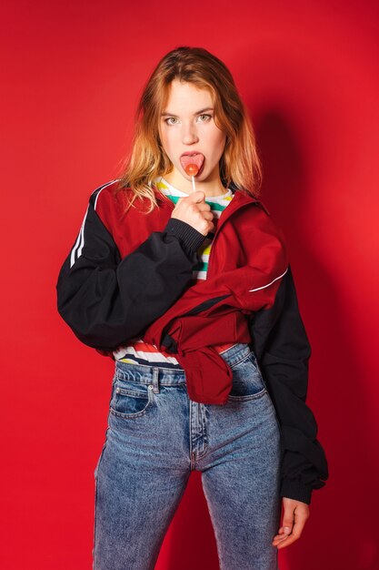 Vibrant portrait of trendy young woman in retro style clothes and lollipop