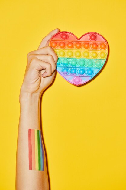 プライド月間lgbtqのシンボルとして黄色の背景に虹の心を持っている女性の手の鮮やかなショット
