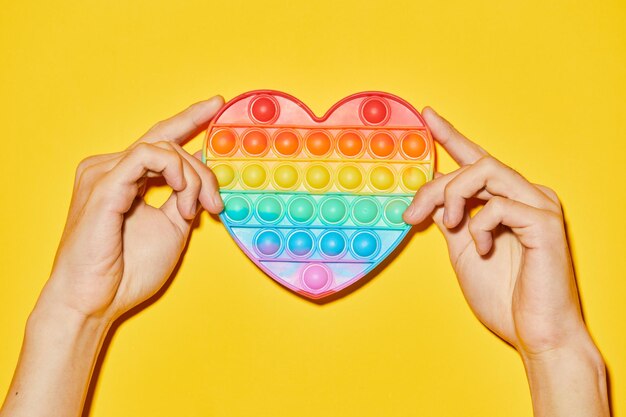 Vibrant shot of female hands holding rainbow heart on yellow background as symbol for pride month lgbtq