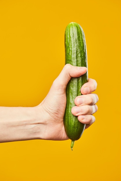 Vibrant shot of hand holding cucumber on yellow background safe sex concept