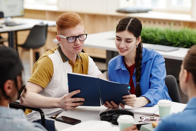 Vibrant shot of two smiling college students reading notes during group discussion in classroom