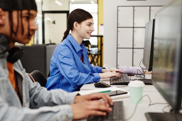 Vibrant side view portrait of smiling young woman using computer in college library while doing rese