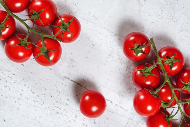 Foto piccoli pomodori rossi vibranti con viti verdi su pietre bianche come una tavola vista dall'alto