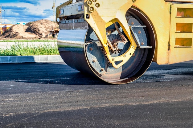 振動ロード ローラーは、建設中の新しい道路にアスファルトを置きます。道路機械の作業のクローズ アップ。都市高速道路の建設工事。