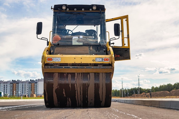 Vibratory road roller lays asphalt on a new road under construction. Close-up of the work of road machinery. Construction work on the construction of urban highways.