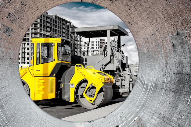 Vibratory road roller lays asphalt on a new road under\
construction closeup of the work of road construction equipment\
modern work on the construction of city streets view from the big\
pipe