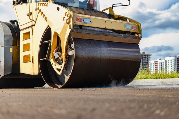 Vibratory road roller lays asphalt on a new road under construction Closeup of the work of road machinery Construction work on the construction of urban highways