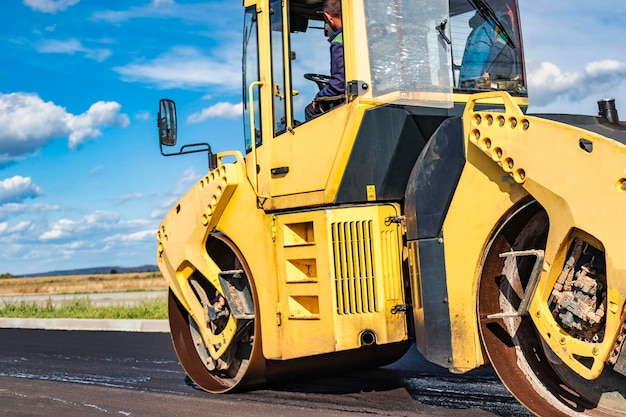 Vibratory road roller lays asphalt on a new road under construction Closeup of the work of road machinery Construction work on the construction of urban highways