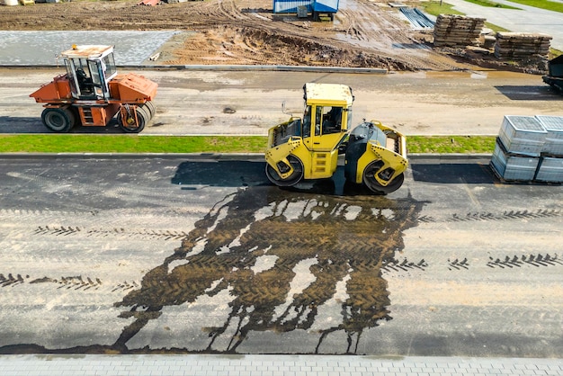 Vibratory road roller lays asphalt on a new road under construction Closeup of the work of road machinery view from above Drone photography Construction work on the arrangement of urban highways