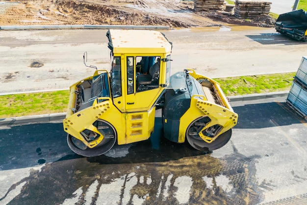 Vibratory road roller lays asphalt on a new road under construction Closeup of the work of road machinery view from above Drone photography Construction work on the arrangement of urban highways