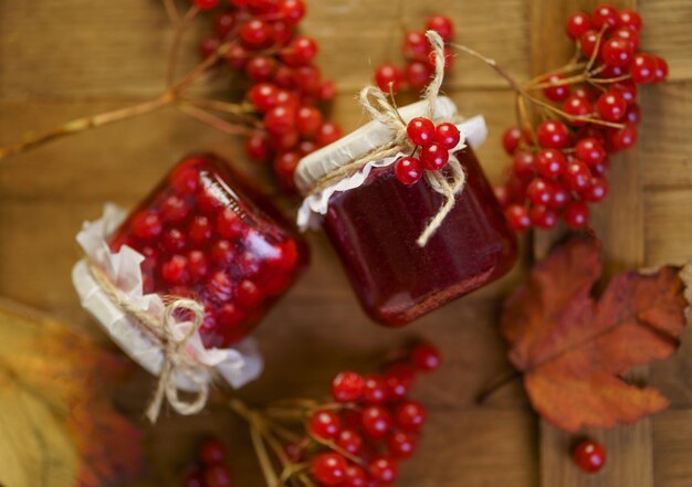 Viburnum jam in a glass jar on a wooden table near fresh viburnum berries