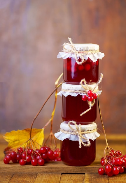 Viburnum jam in a glass jar on a wooden table near fresh viburnum berries