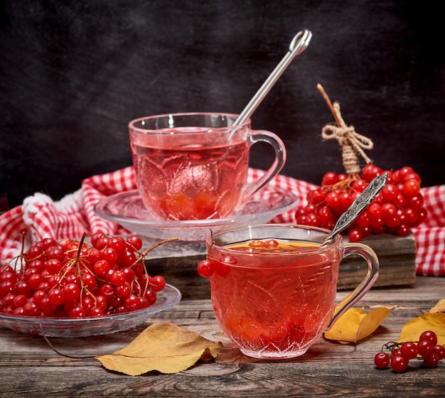 Viburnum tea in a transparent cup with a handle and saucer on a gray wooden table