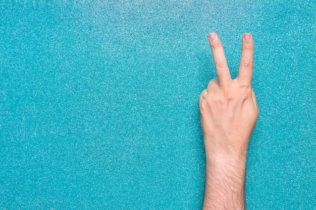 Victory gesture in man hand on turquoise aquamarine background glossy