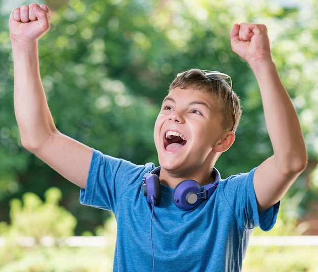 Victory screaming teen boy 1214 year old Winner boy with headphones and sunglasses posing outdoors