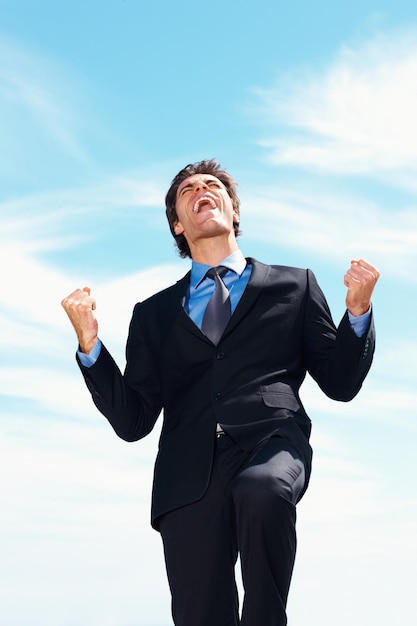 Победа Успешный деловой человек со сжатым кулаком на фоне неба Победа Успешный молодой бизнесмен со сжатым кулаком на фоне неба