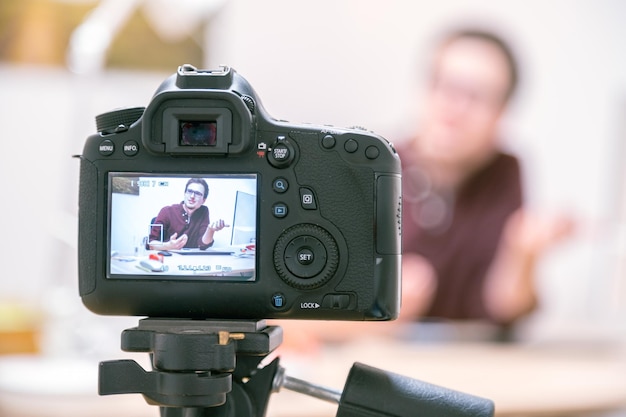 Photo video blogger at home camera on tripod is filming a young man sitting on his working place