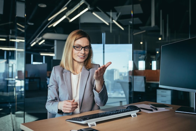 Video call of a happy and successful business woman an employee
has an online meeting advises employees looks at the webcam and
cheerfully explains gesturing with her hands