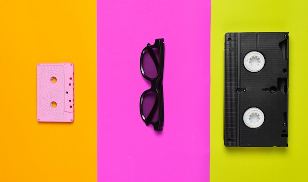 Video cassette, sunglasses, audio cassette on a multi-colored paper.