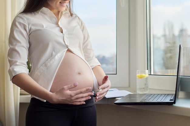화상 채팅, 전화, 노트북 웹캠에 큰 배를 보여주는 임신한 행복한 여성. 온라인 커뮤니케이션, 원격 근무, 임신부 격리 작업
